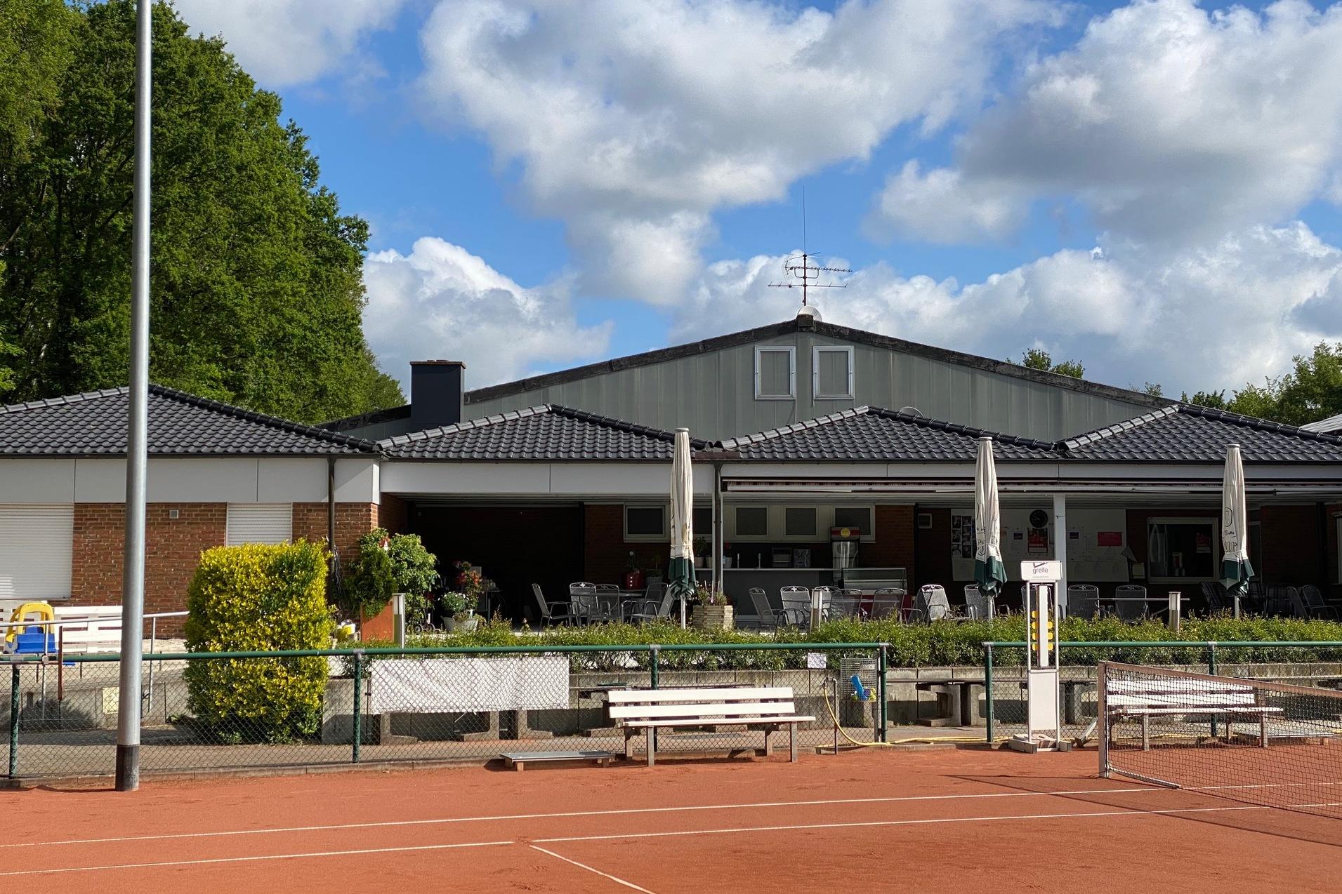 Tennisplatz mit einem Vereinsgeb&auml;ude im Hintergrund und Sonnenschirmen auf der Terrasse, umgeben von B&auml;umen und Wolken.