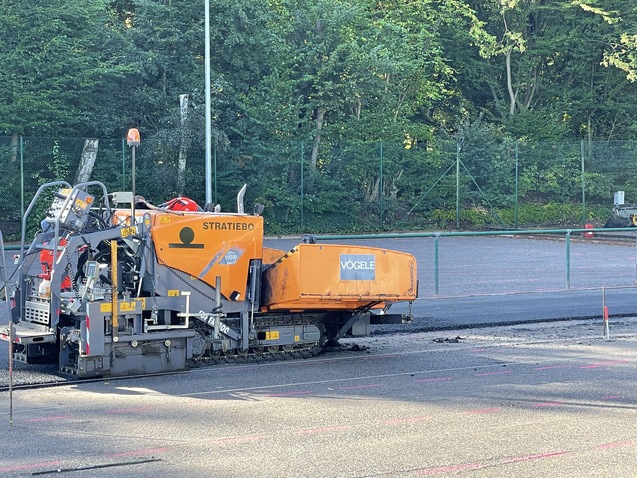 Baumaschine zum Asphaltieren auf einer Baustelle mit gr&uuml;ner Vegetation im Hintergrund.