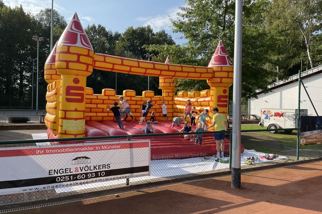 Bunte H&uuml;pfburg in Form einer Burg mit Kindern, die darauf spielen, im Hintergrund ein Werbebanner.