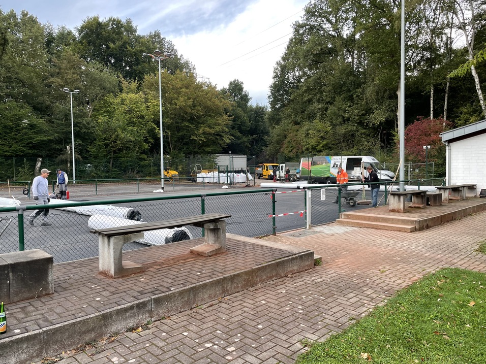 Blick auf einen Sportplatz mit Sanierungsarbeiten, umgeben von B&auml;umen und Sitzb&auml;nken aus Stein.
