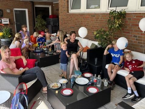 Gruppe von Erwachsenen und Kindern in einem gemütlichen, überdachten Außenbereich mit Snacks und Getränken.