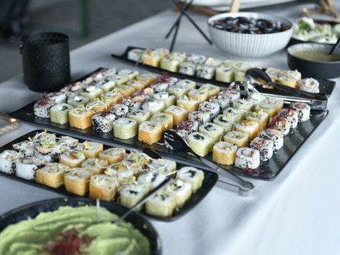 Anordnung verschiedener Sushi-Rollen auf dunklen Platten neben einer Sch&uuml;ssel mit Wasabi und einer weiteren Speise.