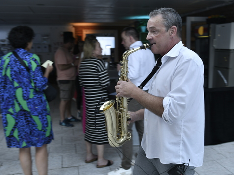 Mann mit Saxophon spielt in einem belebten Raum, umgeben von Menschen in informeller Kleidung.