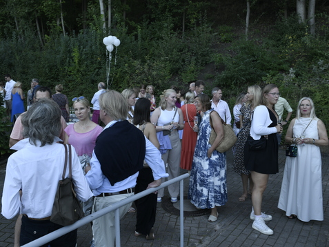 Gruppe von Menschen in festlicher Kleidung bei einer Veranstaltung im Freien, umgeben von B&auml;umen und Dekoration.