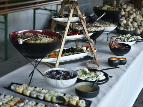 Buffet mit verschiedenen Salaten, Sushi, Dips und Br&ouml;tchen auf einem Tisch in einem festlichen Ambiente.