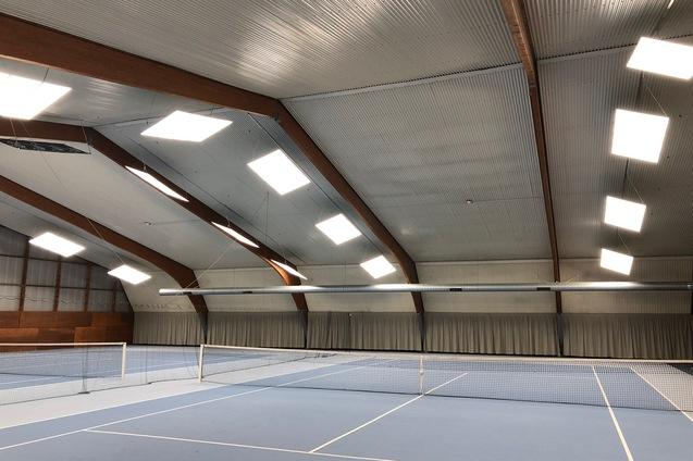 Blick in eine Tennis-Halle mit blauem Boden, Netzen und gro&szlig;en Dachfenstern.