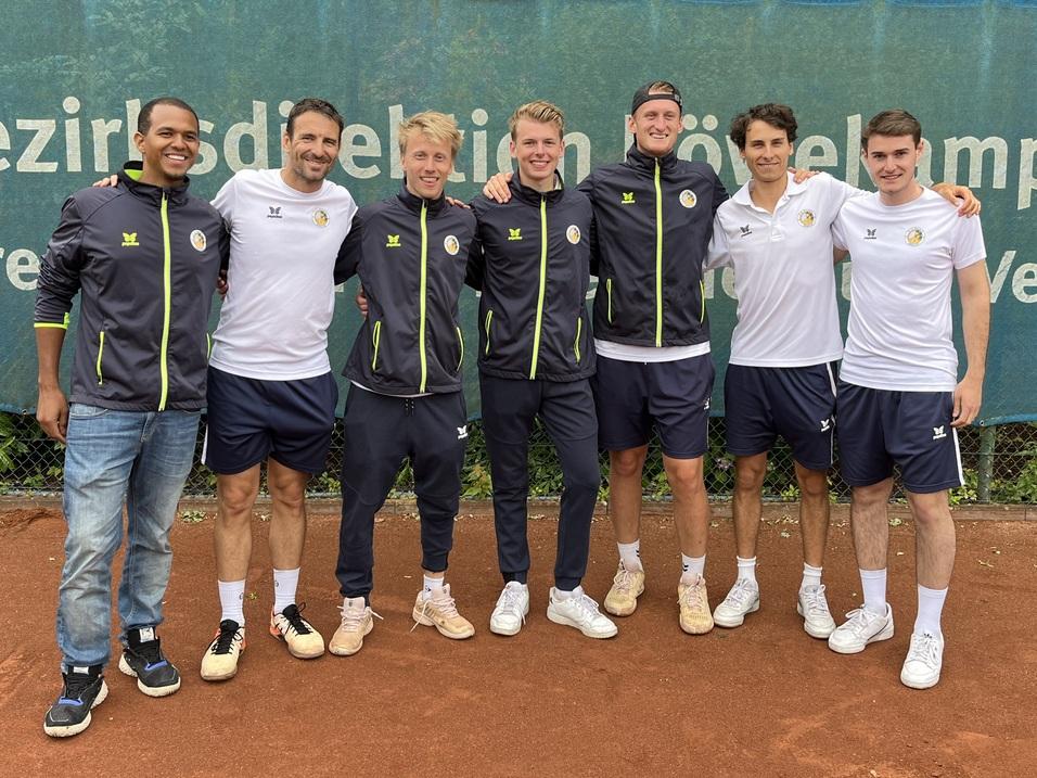 Gruppenfoto von acht M&auml;nnern in Sportkleidung auf einem Tennisplatz, im Hintergrund eine Werbetafel.