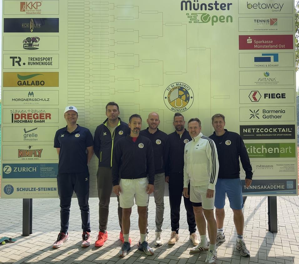 Gruppe von sechs Personen in Sportkleidung vor einem gro&szlig;en Werbeplakat des M&uuml;nster Open-Turniers.