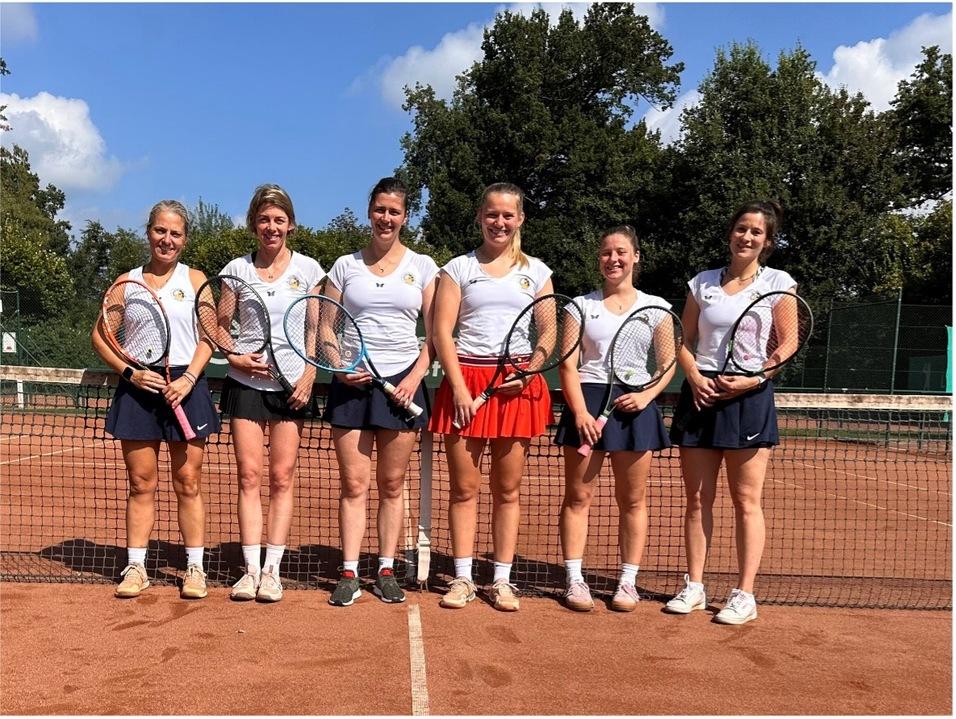 Sechs Tennisspielerinnen stehen l&auml;chelnd auf einem Sandplatz, jeweils mit einem Schl&auml;ger in der Hand, im Hintergrund B&auml;ume.