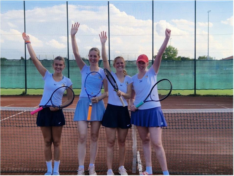 Vier junge Frauen in Tenniskleidung posieren auf einem Tennisplatz und halten Schl&auml;ger in die H&ouml;he.