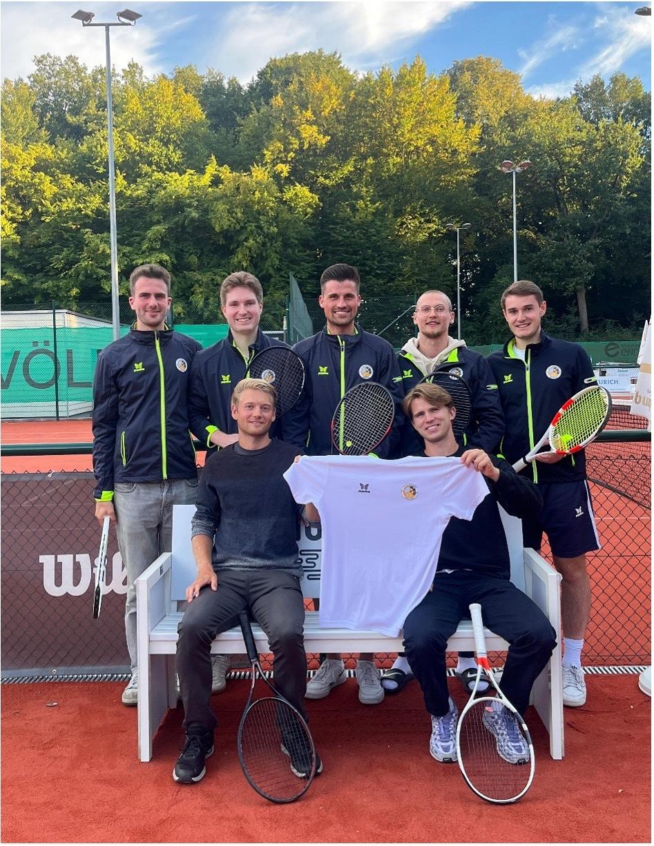 Gruppe von sechs Tennis-Spielern steht und sitzt auf einer Bank, mit Schl&auml;gern und einem Trikot in der Hand.