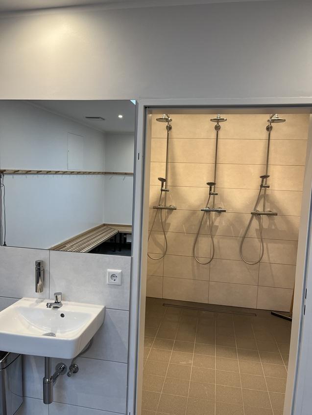 Blick in einen modern gestalteten Sanitärbereich mit Waschbecken und drei Duschbereichen.