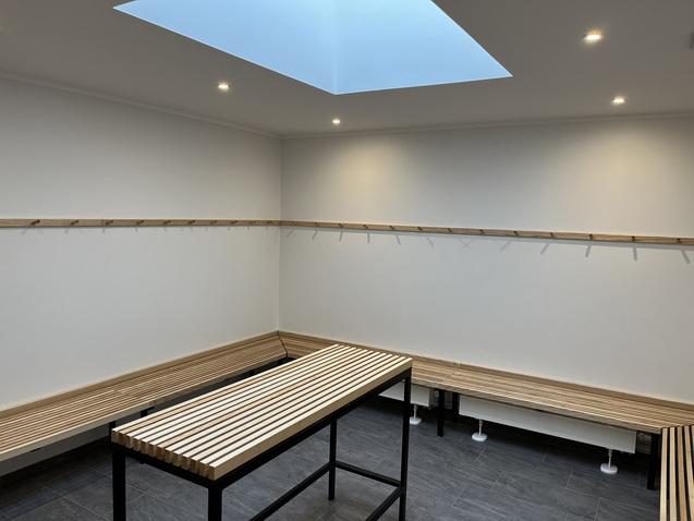 Helle Umkleidekabine mit Holzbänken, einem Tisch und einer Dachluke für Tageslicht.
