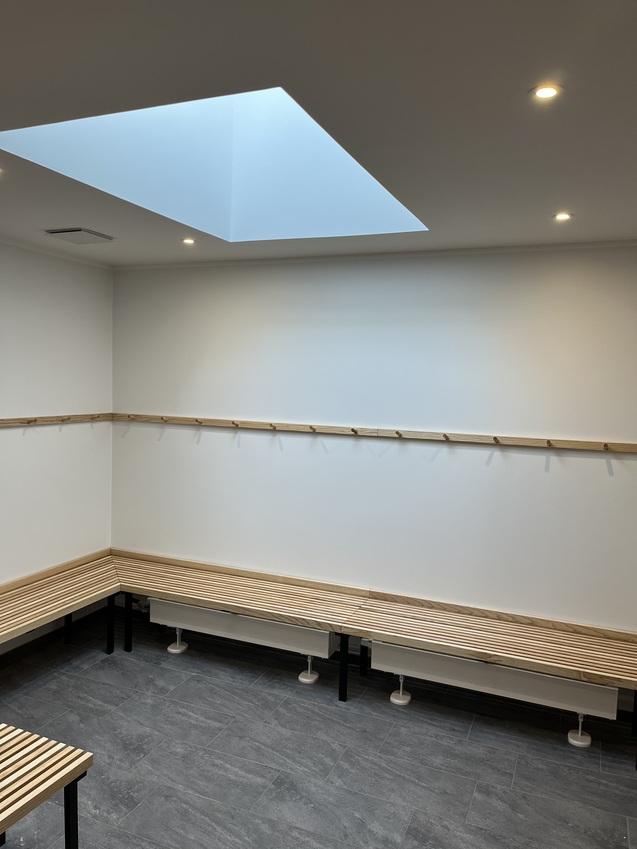 Lichtdurchfluteter Umkleideraum mit Holzbänken und einer Dachluke über dem Raum.