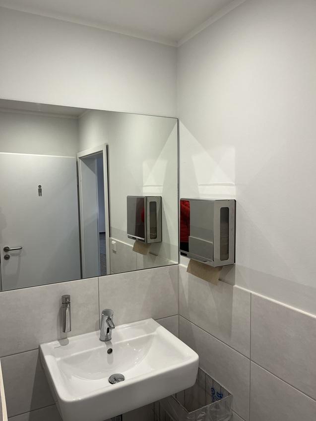 Blick in ein modernes Badezimmer mit Waschbecken, Spiegel, Seifenspender und gespannter Handtuchrolle an der Wand.