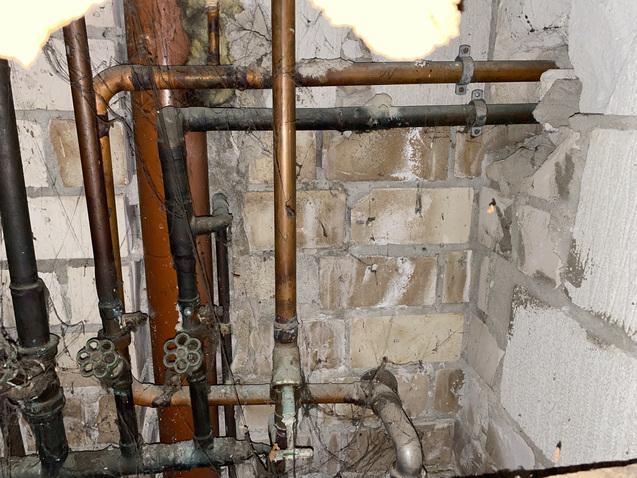 Verwobenes Rohrleitungssystem aus Kupfer und Kunststoff an einer gemauerten Wand in einem Keller.