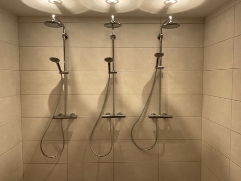 Drei Duschkopf-Anlagen an einer hellen Fliesenwand in einem modernen Badezimmer.