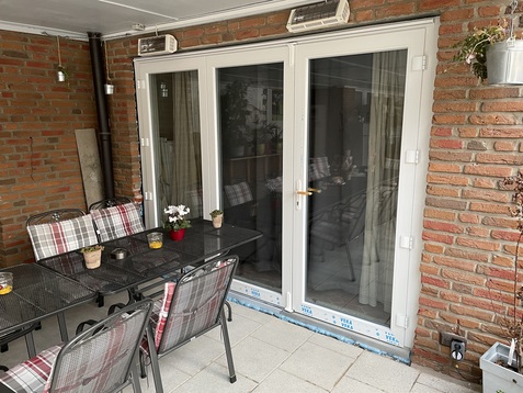 Terrasse mit Tisch und St&uuml;hlen, davor doppelte Glast&uuml;ren und Backsteinwand, dekoriert mit Pflanzen.
