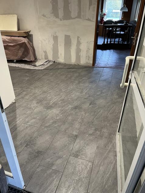 Blick auf einen grauen gefliesten Boden in einem Raum mit unvollständigen Wänden und einem weiteren Raum im Hintergrund.