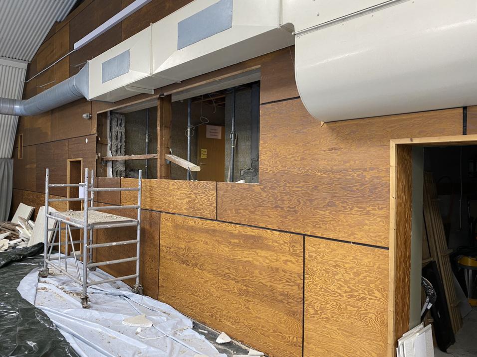 Bauarbeiten an einer Wand mit Holzverkleidung, sichtbare Baugerüste und Lärm- und Schutzmaterialien auf dem Boden.
