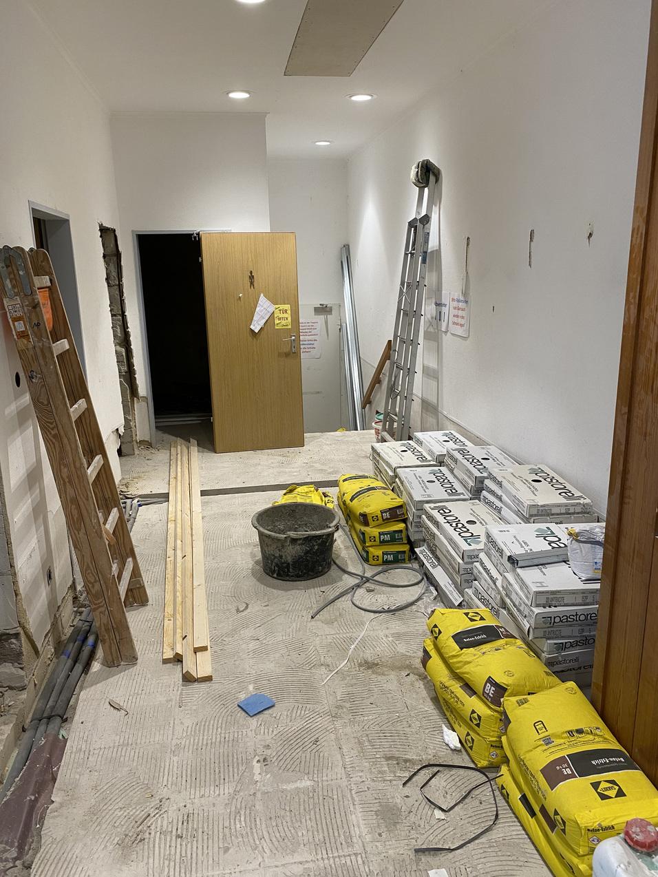 Blick in einen renovierungsbedürftigen Flur mit Leitern, Baustellenmaterial und einem offenen Türenbereich.