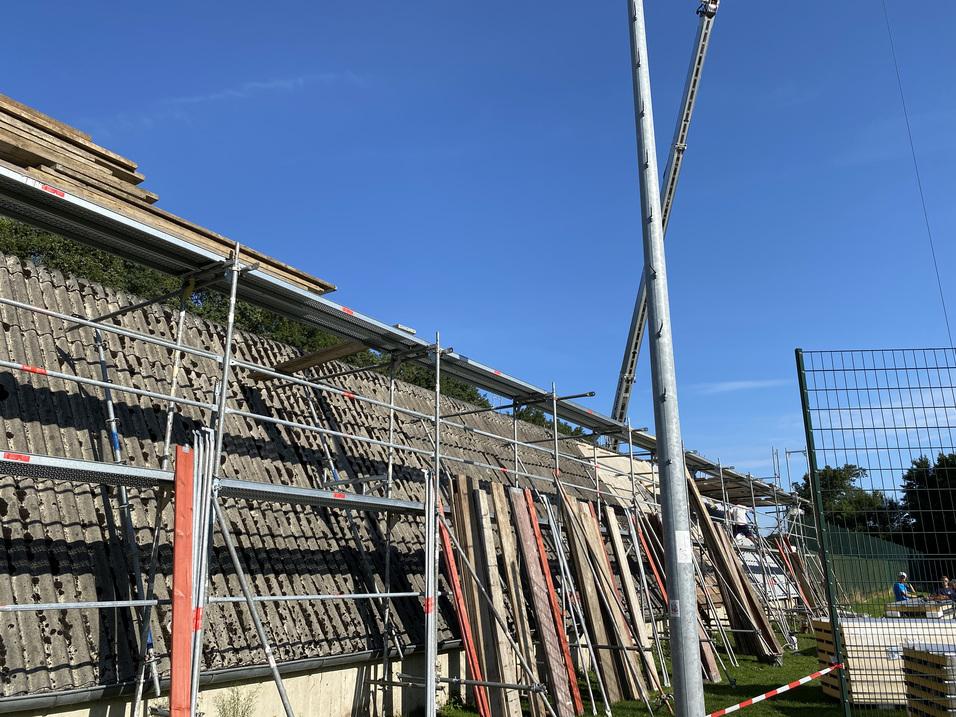 Baugerüst neben einer Mauer, mit Holzplatten zur Baustelle und blauem Himmel im Hintergrund.