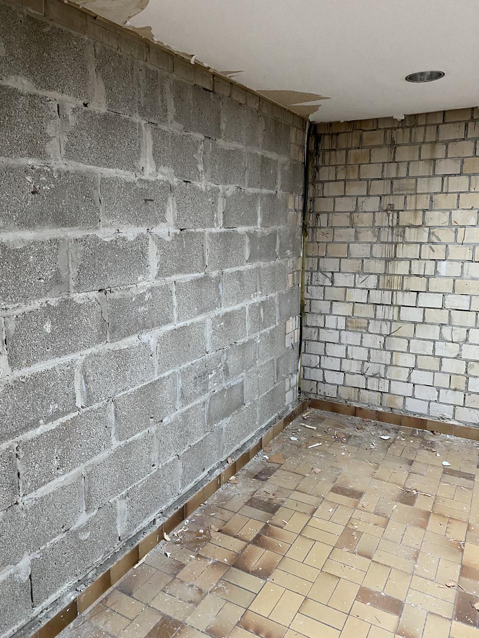 Rohbau mit einer grauen Mauer aus Betonsteinen und einer verputzten Steinwand in einem unvollendeten Raum.