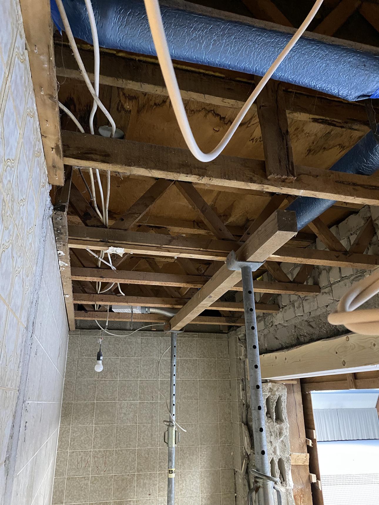 Blick auf einen unvollendeten Raum mit Holzgerüst, Leitungen und einem provisorischen Licht über einem Fliesenboden.