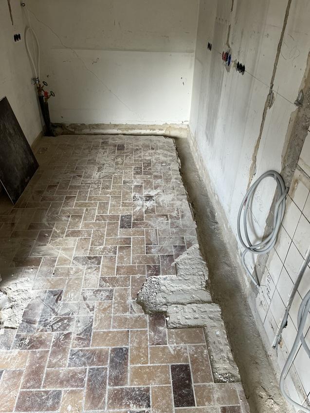 Blick auf einen unvollendeten Raum mit einem gefliesten Boden, einer Wand ohne Verkleidung und sichtbaren Leitungen.