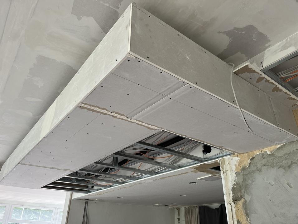 Deckeninstallation aus Gipskartonplatten mit sichtbarem Stahlrahmen und elektrischen Kabeln in einem unvollendeten Raum.
