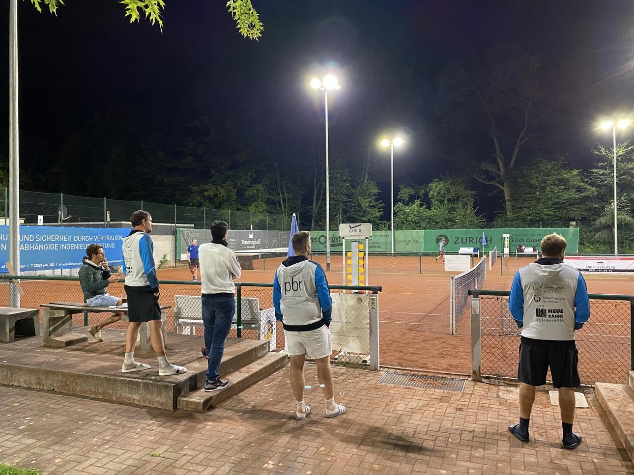 Gruppenschiedsrichter beobachten ein Tennismatch auf einem beleuchteten Platz bei Nacht.