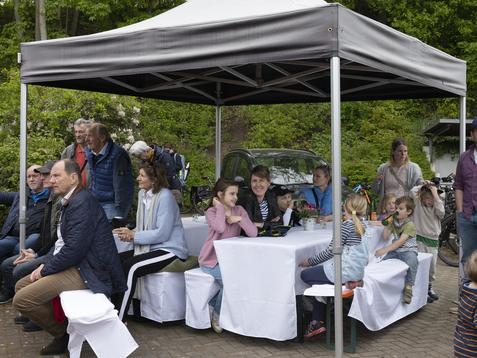 Menschen sitzen unter einem Pavillon, umgeben von B&auml;umen, w&auml;hrend sie an Tischen entspannen.