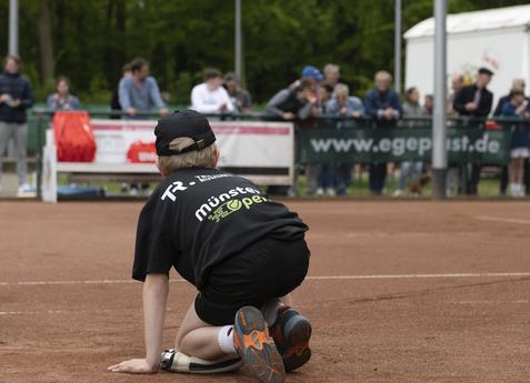 Junge kniet auf einem Tennisplatz und schaut zum Netz, Zuschauer im Hintergrund beobachten das Spiel.