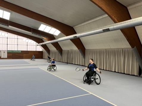 Rollstuhltennisspieler in einer Sporthalle, die auf einem blauen Platz Tennis spielen. Hintergr&uuml;nde mit Vorh&auml;ngen.