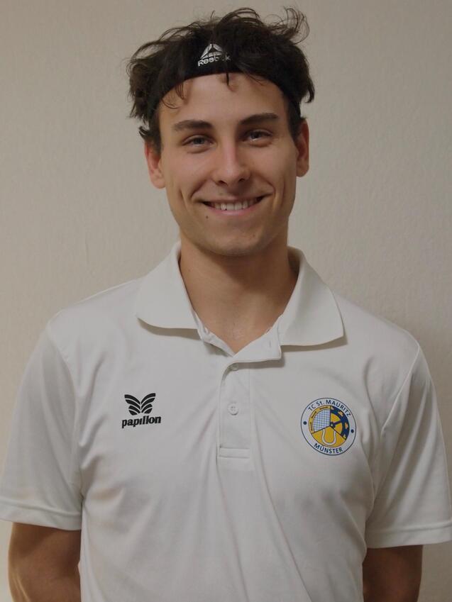 L&auml;chelnder junger Mann in wei&szlig;em Poloshirt mit Vereinslogo und Kopfband vor neutralem Hintergrund.