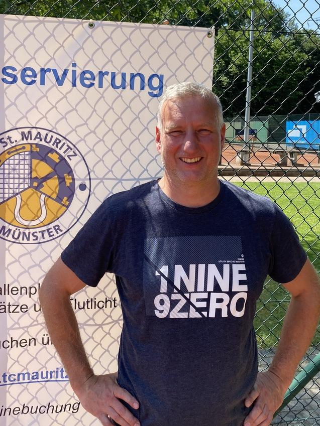 Mann mit kurzem Haar steht vor einem Tennisplatz und einem Schild zur Platzreservierung in M&uuml;nster.