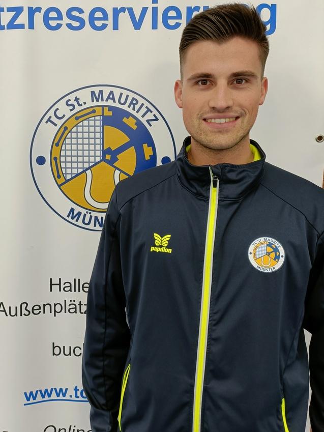 L&auml;chelnder Mann in Sportjacke vor einem Banner mit dem Logo des TC St. Mauritz M&uuml;nster und Informationen zur Platzreservierung.